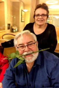 Elderly couple smiling with man holding a rose in his mouth in a senior living unit.