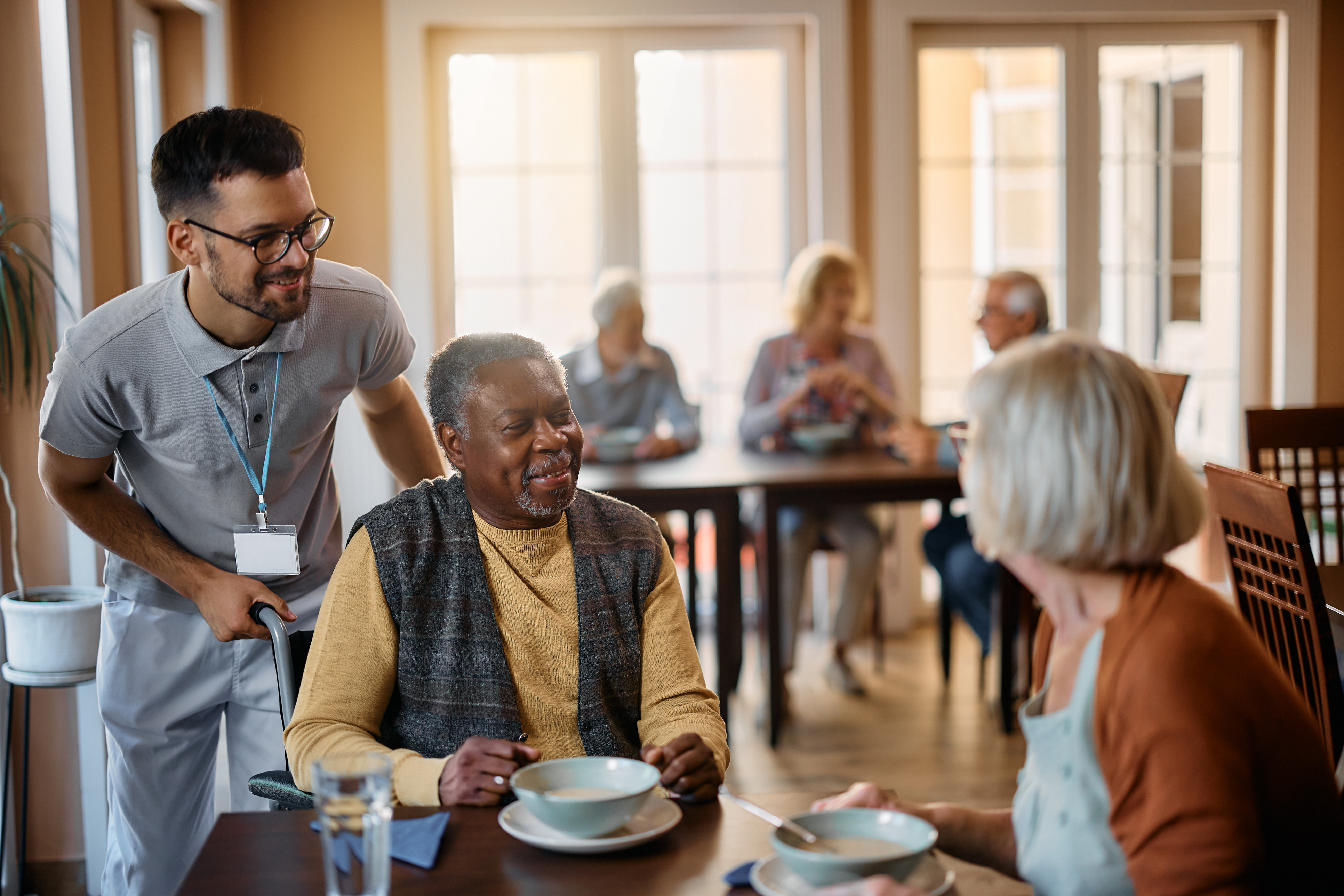 Happy senior people and their caregiver talking in dining room at nursing home.