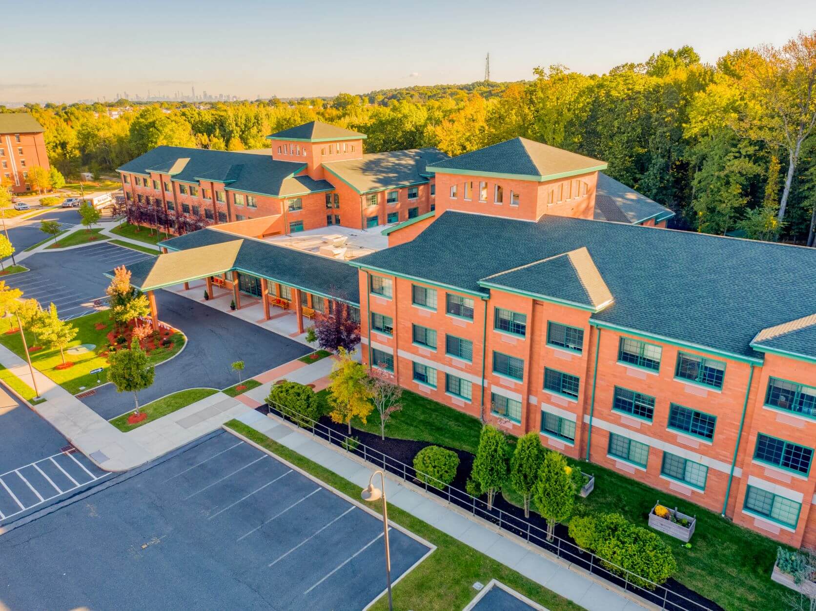 Aerial view of a three-story senior living community surrounded by trees with spacious parking.