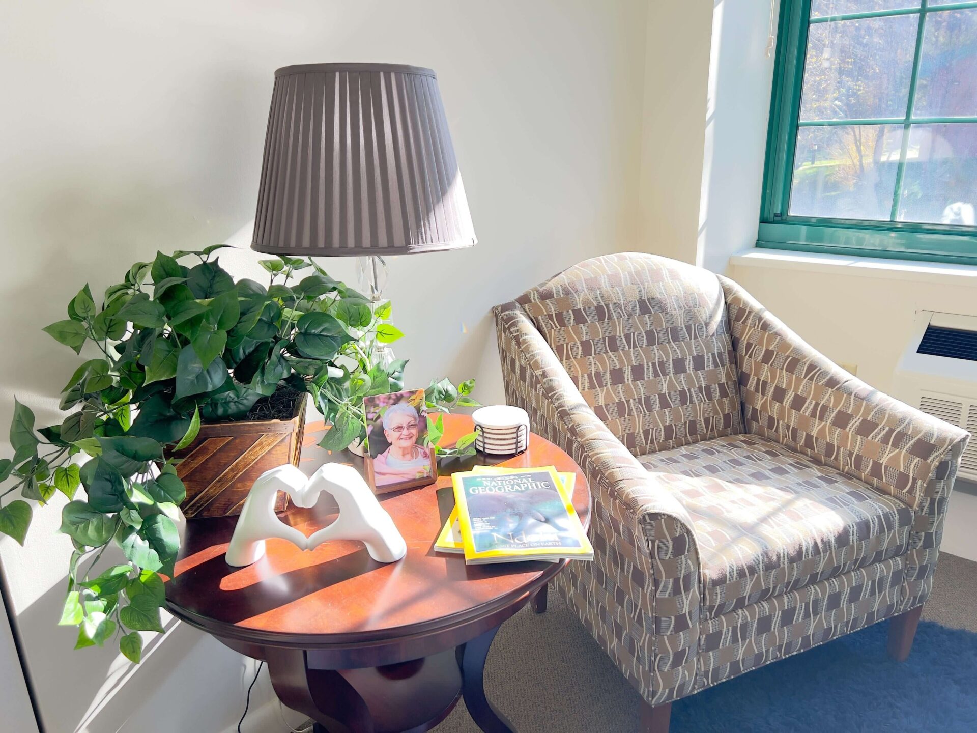 Cozy Reading Nook in Senior Living Community Cozy reading nook with chair, table lamp, plant, books, and photo in a senior living community.