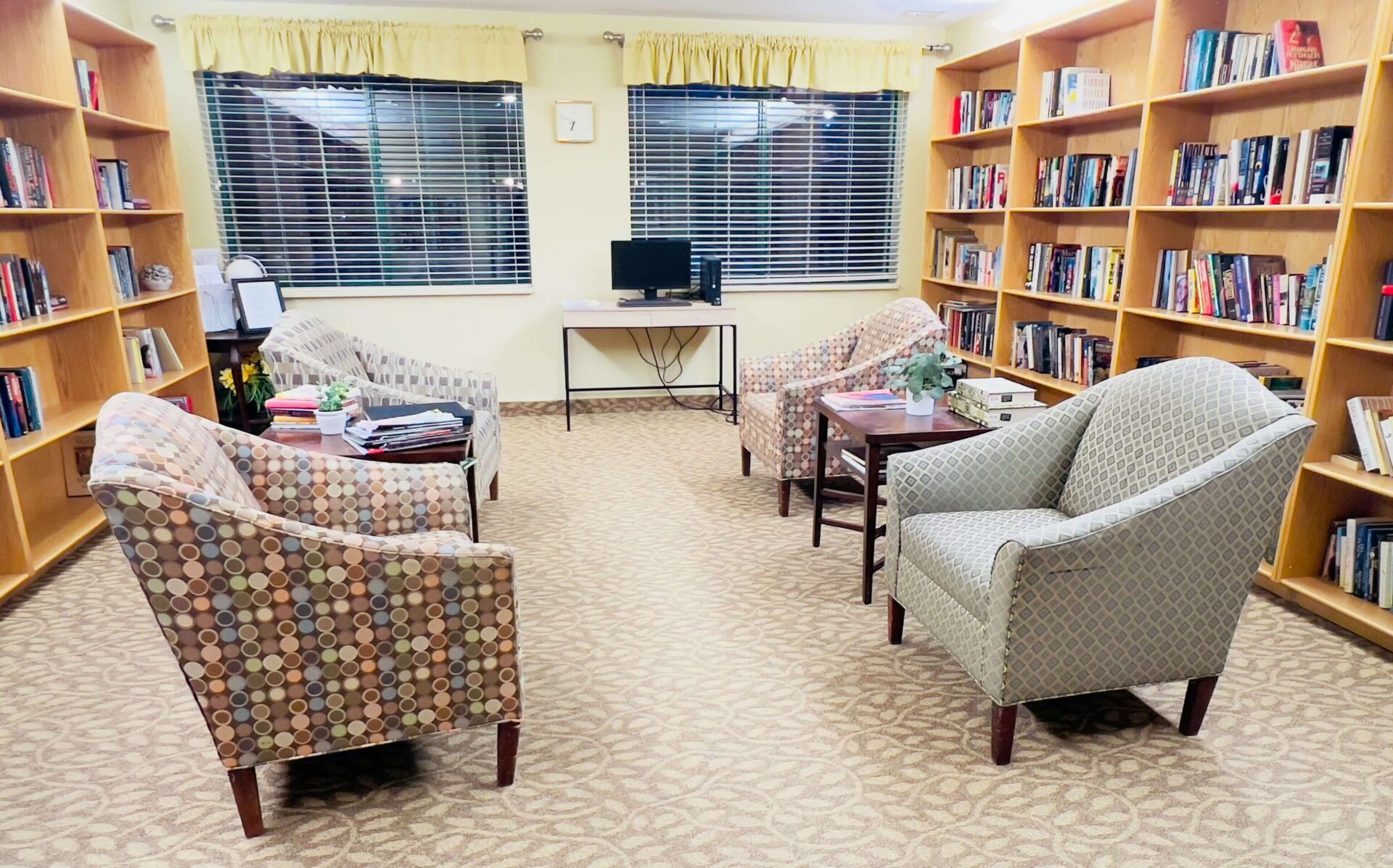 Comfortable reading room with patterned armchairs, bookshelves, and a computer desk.