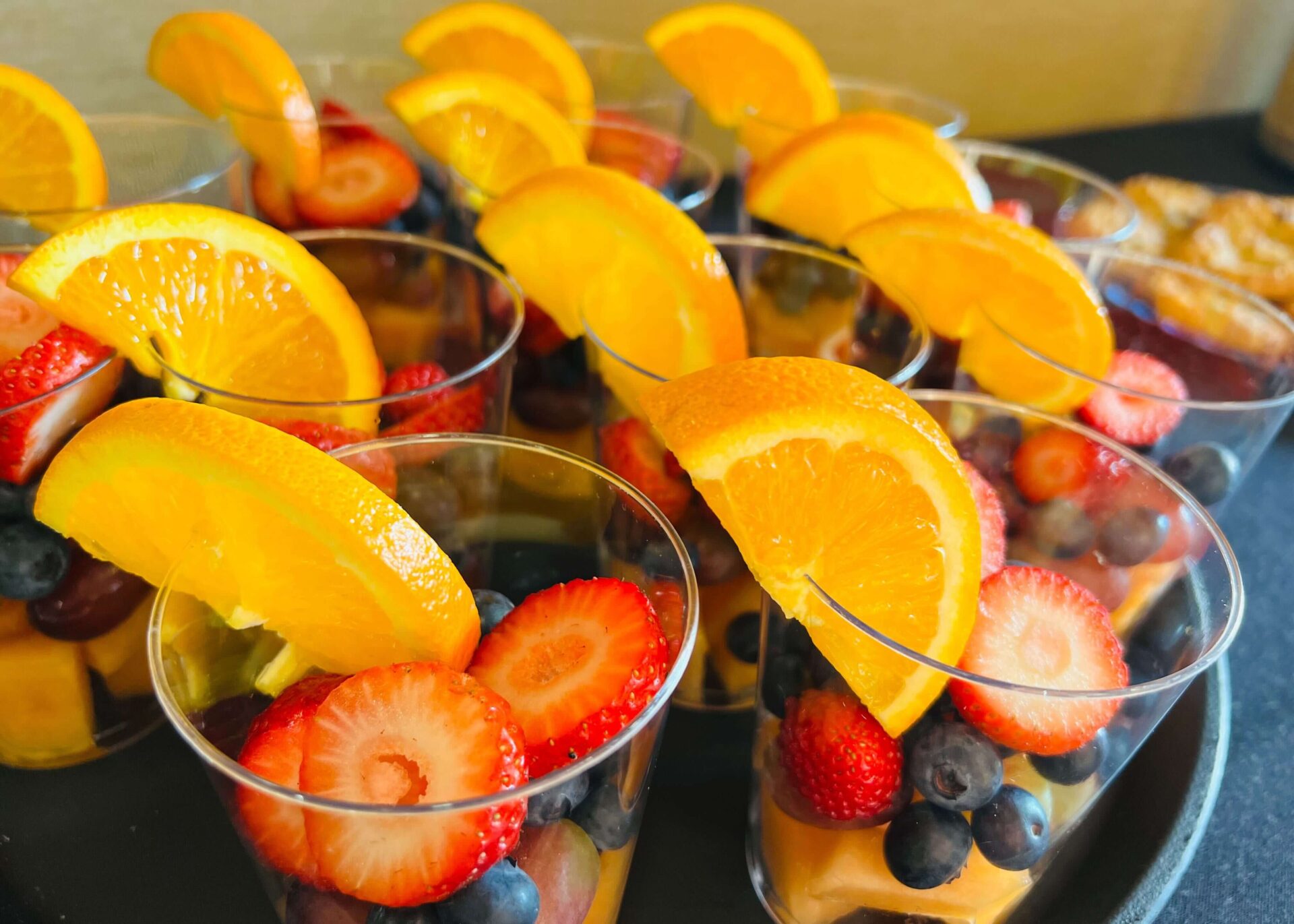 Plastic cups filled with fresh blueberries, strawberries, and orange slices on a tray.