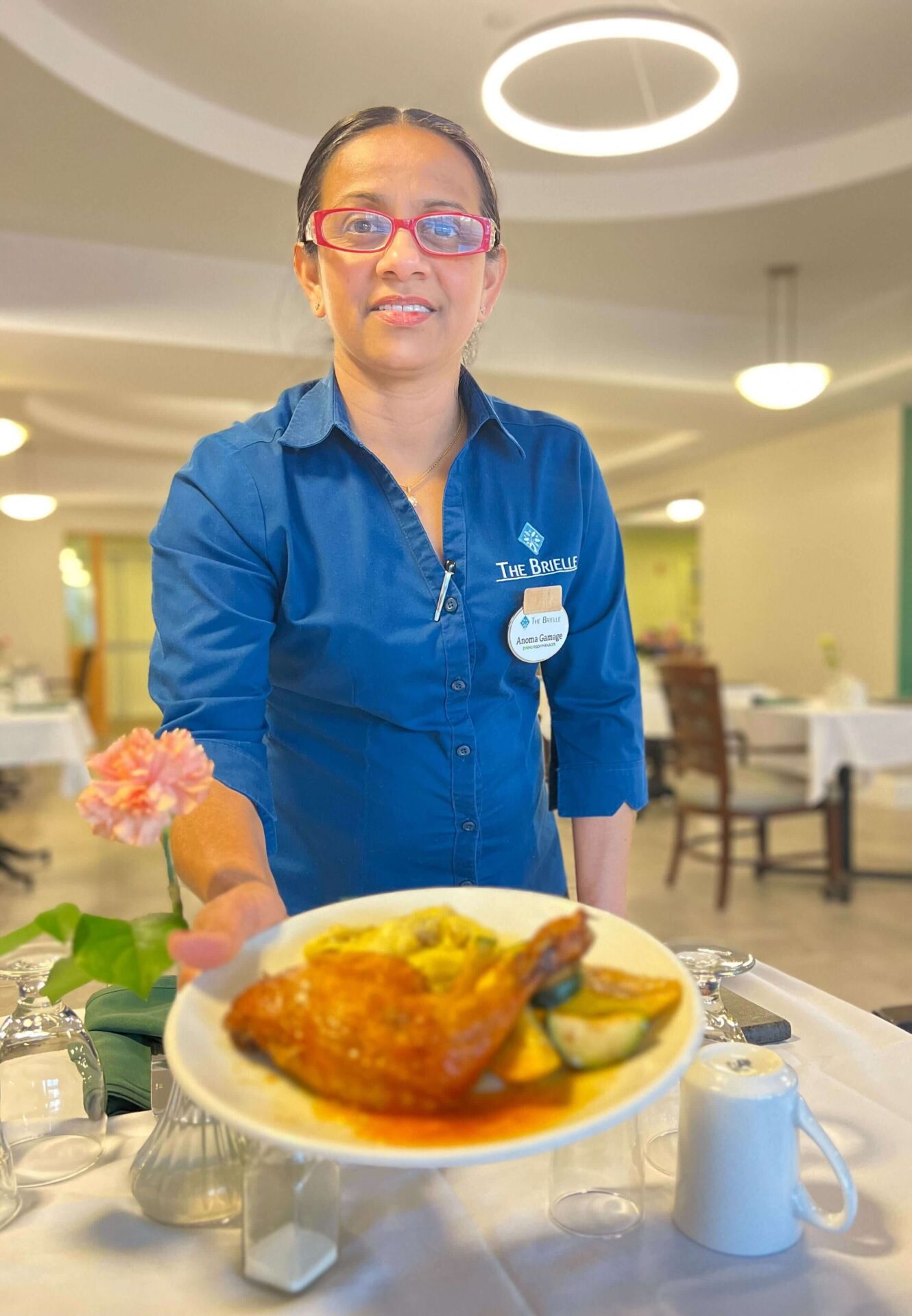 Server in blue uniform offers a plate of food at a senior living community dining area.