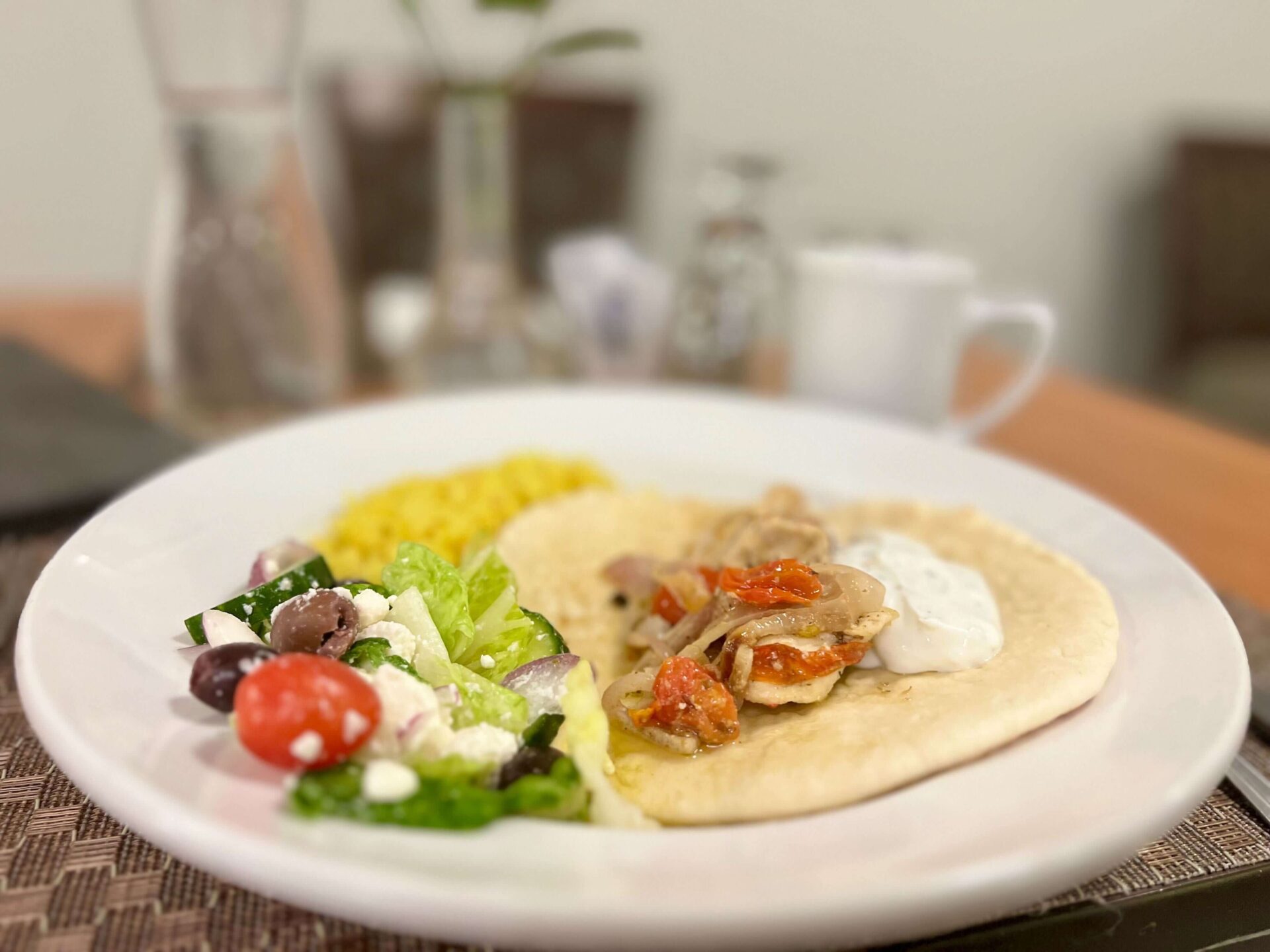 A Greek meal with salad, yellow rice, and flatbread topped with meat and vegetables on a white plate.
