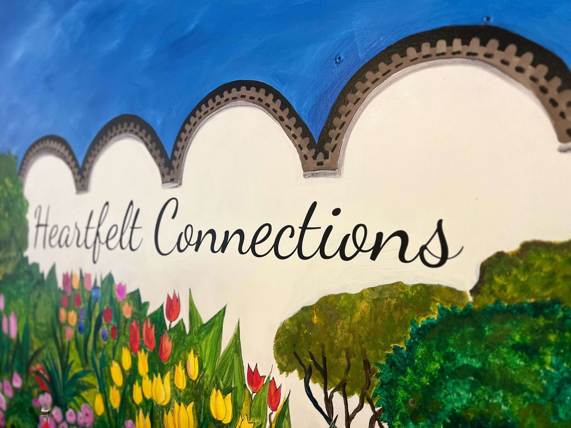 Mural with Heartfelt Connections text, colorful flowers, greenery, and a blue sky background.