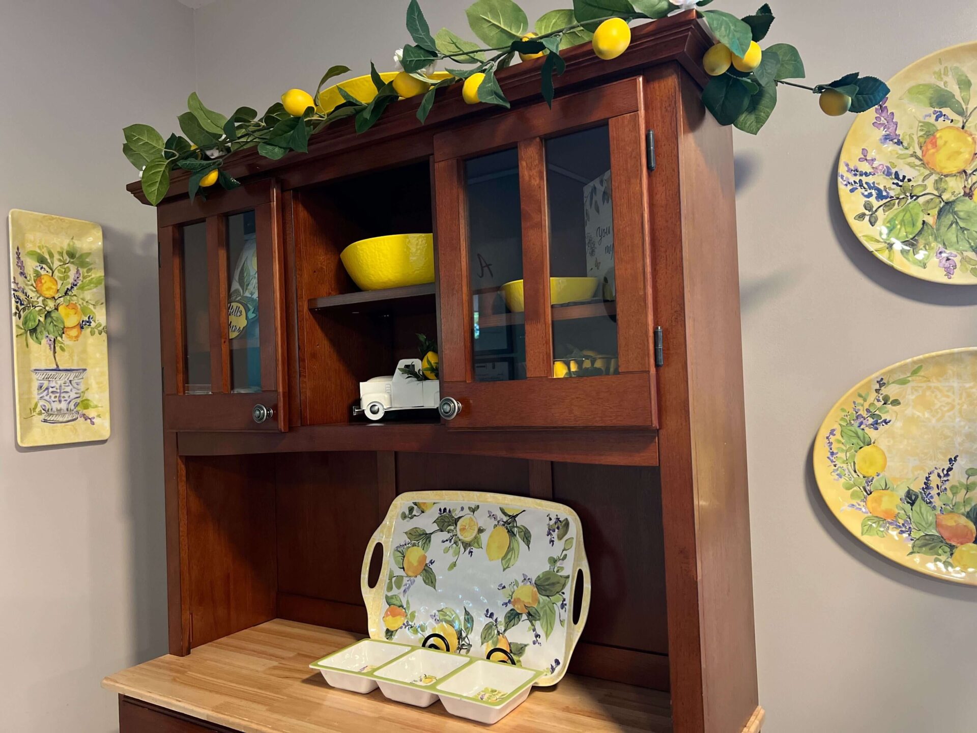 Wooden kitchen hutch with lemon-themed decorations, yellow dishes, and vibrant wall art.