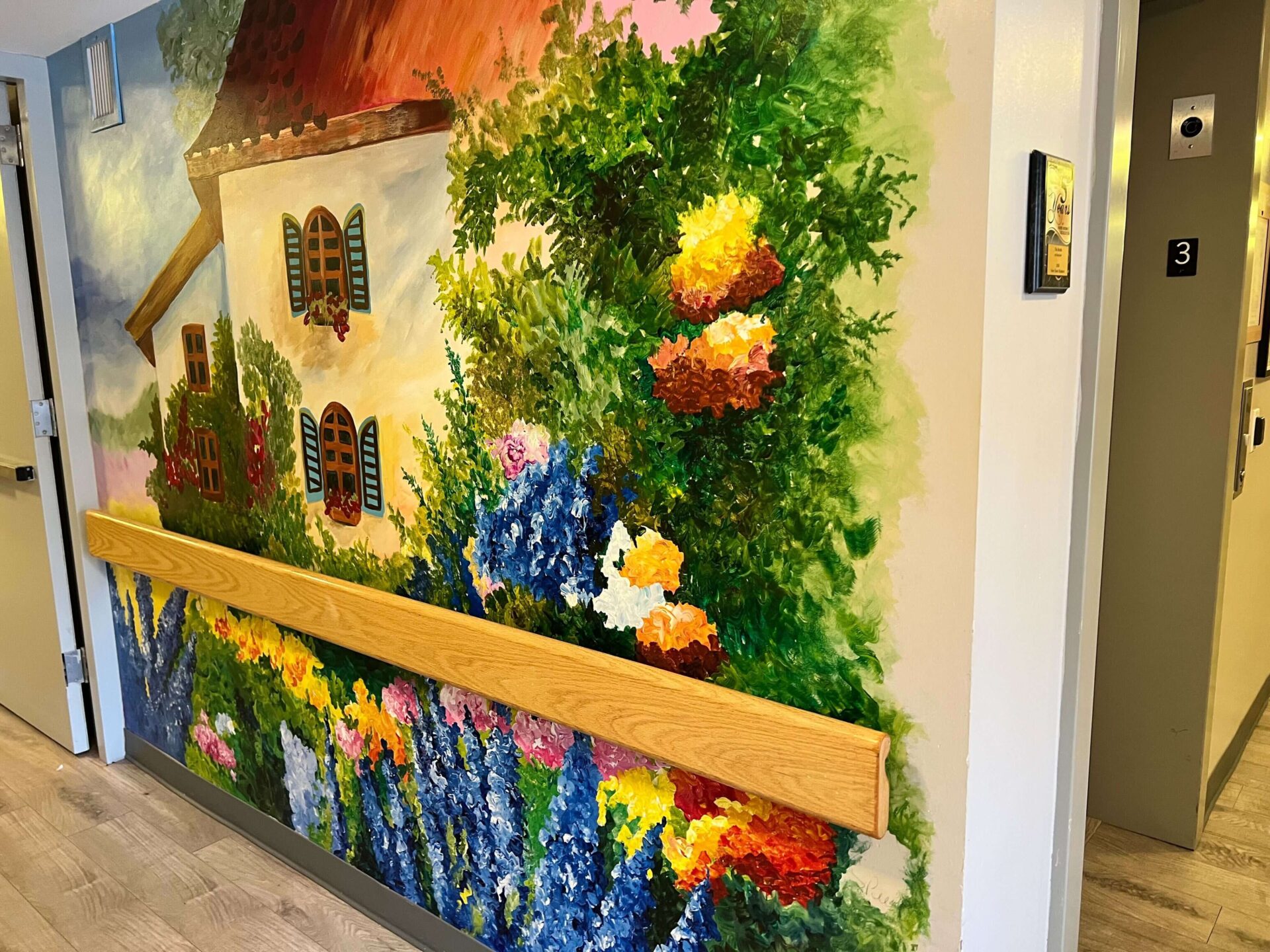 Colorful mural of a house with vibrant flowers on the wall of a hallway next to unit door number 3.