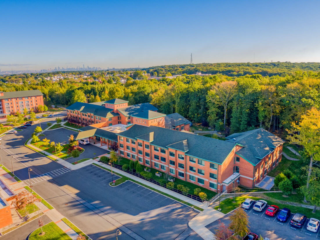 Aerial view of a senior living community surrounded by trees and situated near a sprawling cityscape.