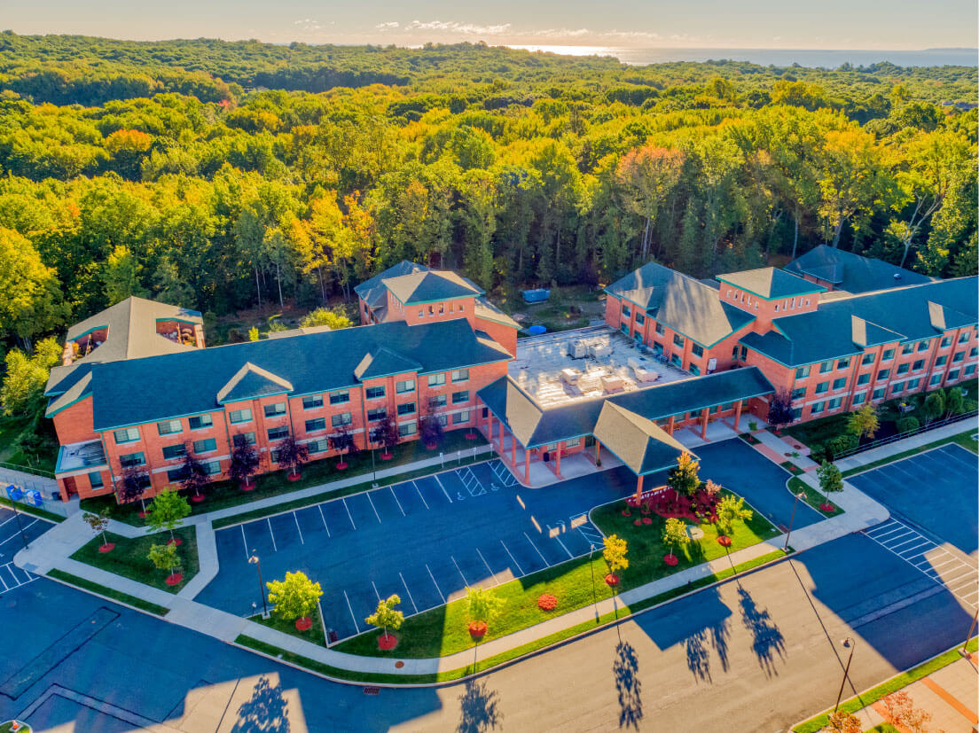 Aerial view of a well-maintained, brick-built senior living community surrounded by lush green trees.