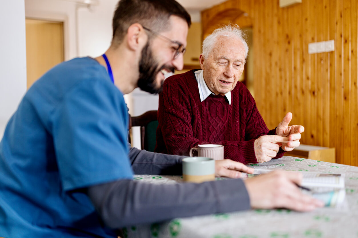 Senior man and caregiver discussing a magazine over coffee in a cozy unit.