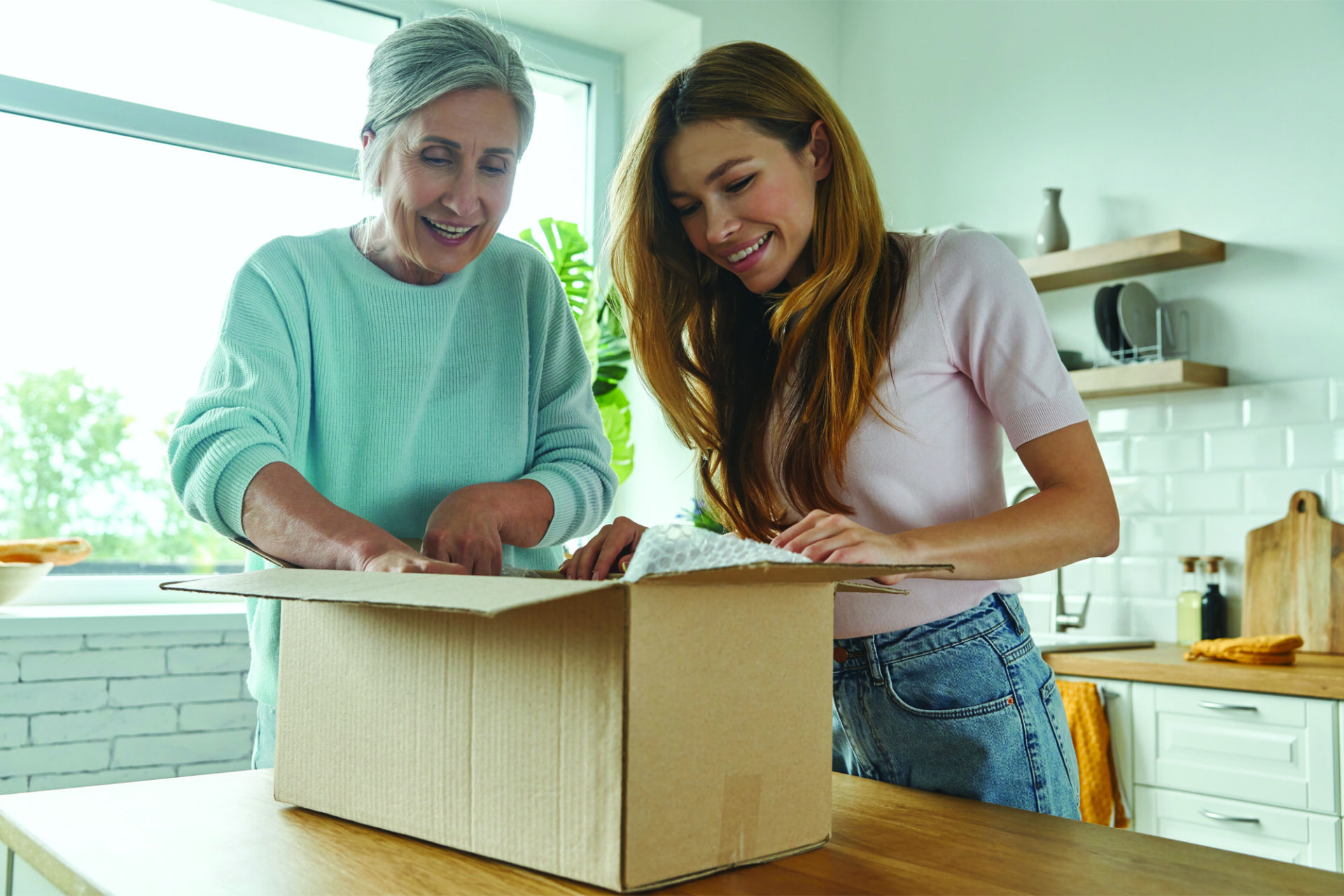 Two women smiling as they unpack a moving box together on a kitchen counter