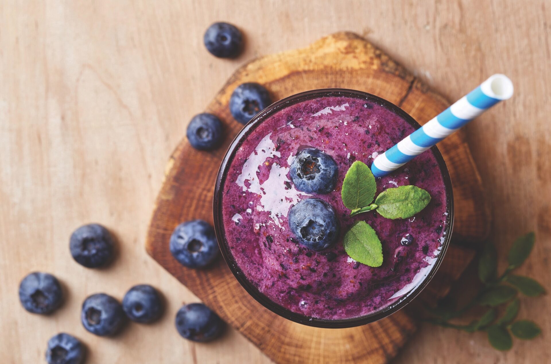 Blueberry smoothie with a striped straw, topped with fresh blueberries and mint